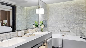 A modern bathroom with two sinks, a large mirror, a bathtub, and marble walls.