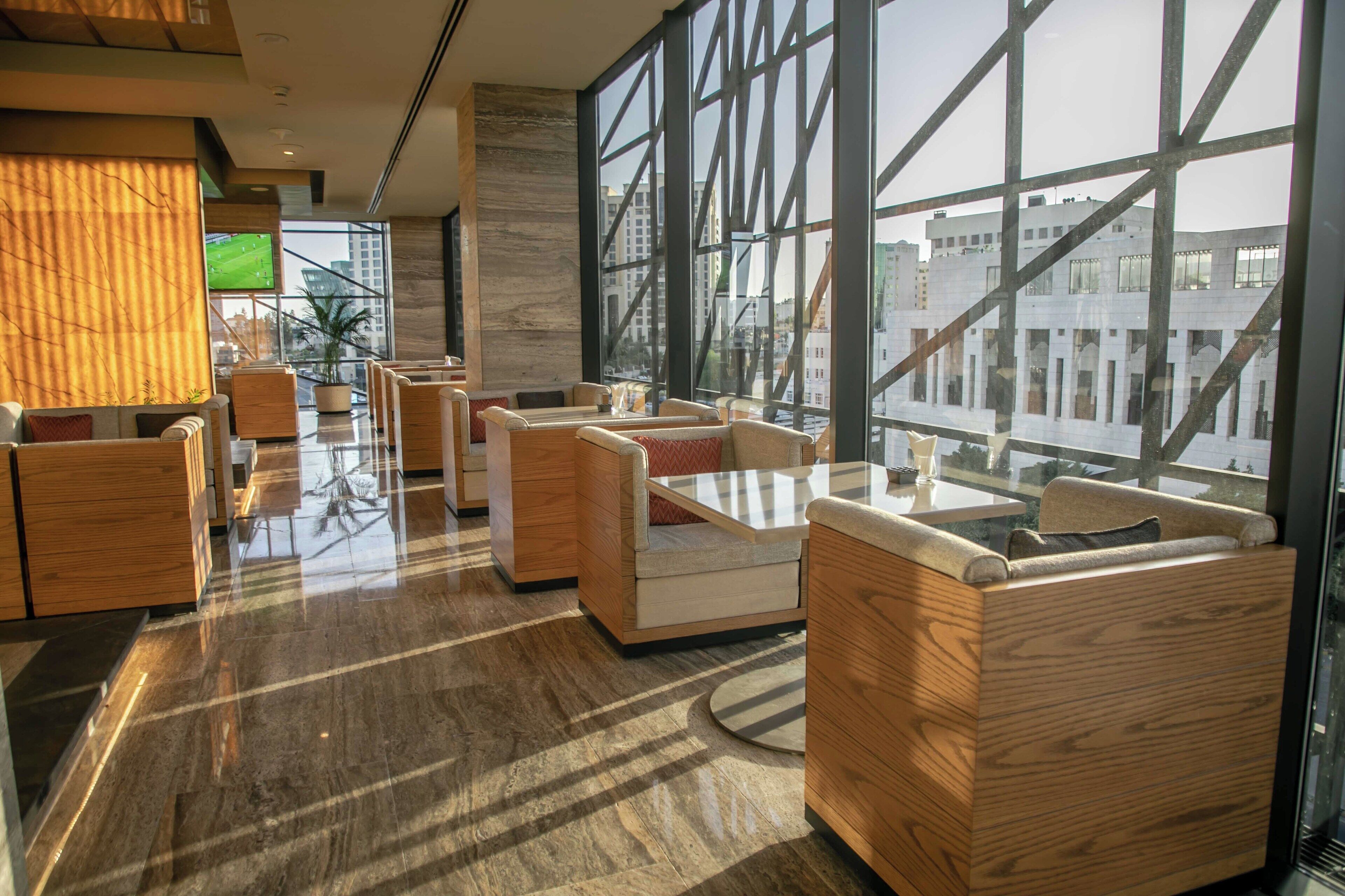 A modern hotel lobby with wooden furniture, large windows, and a flat-screen TV.