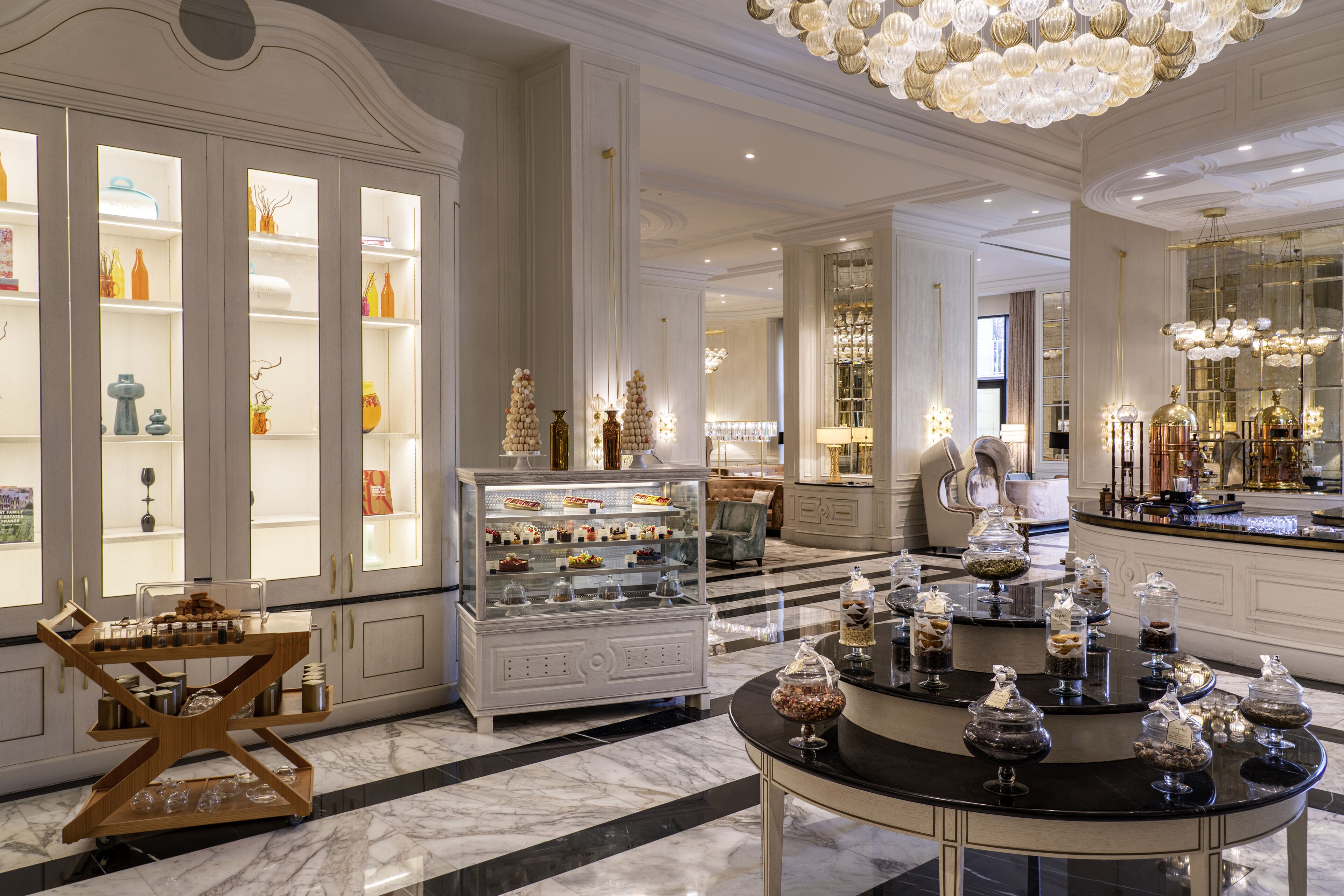 A luxurious hotel lobby with marble flooring, elegant chandeliers, and a central display of desserts.