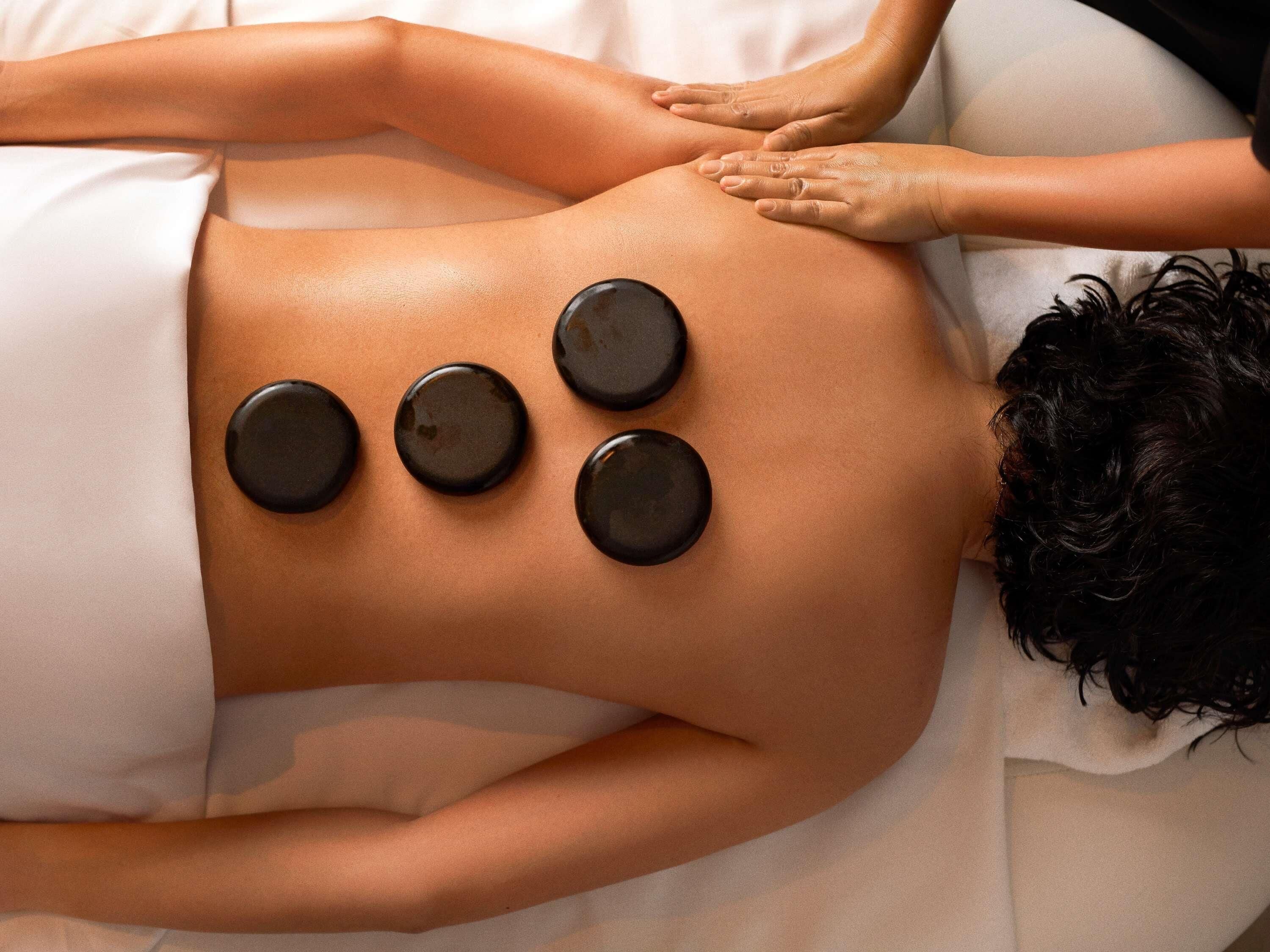 A person receiving a back massage with four black stones placed on their back.