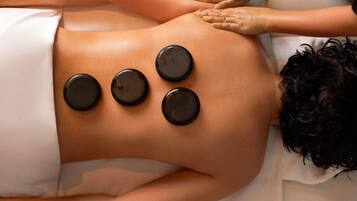 A person receiving a back massage with four black stones placed on their back.