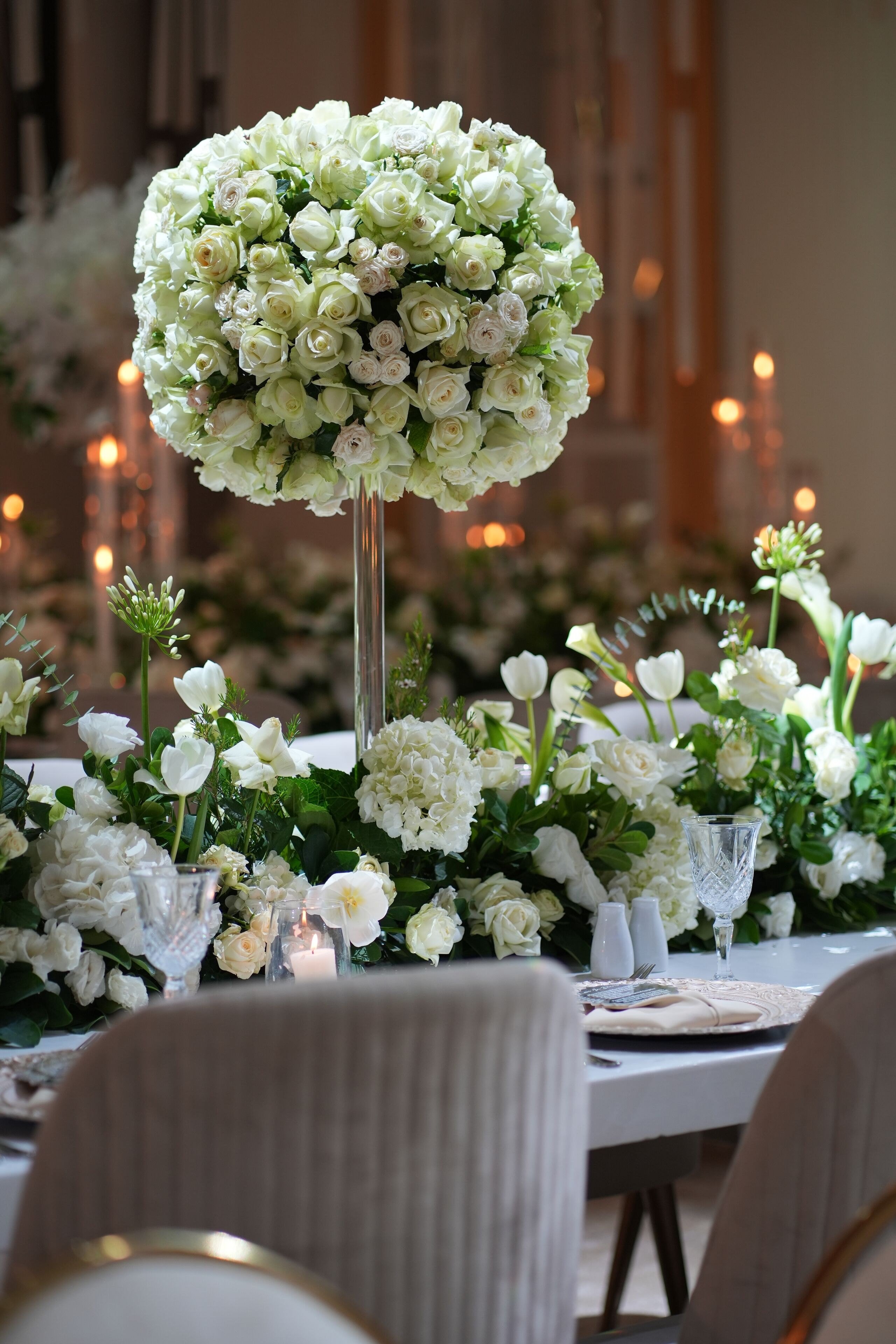 A table set with white flowers, candles, and glassware.