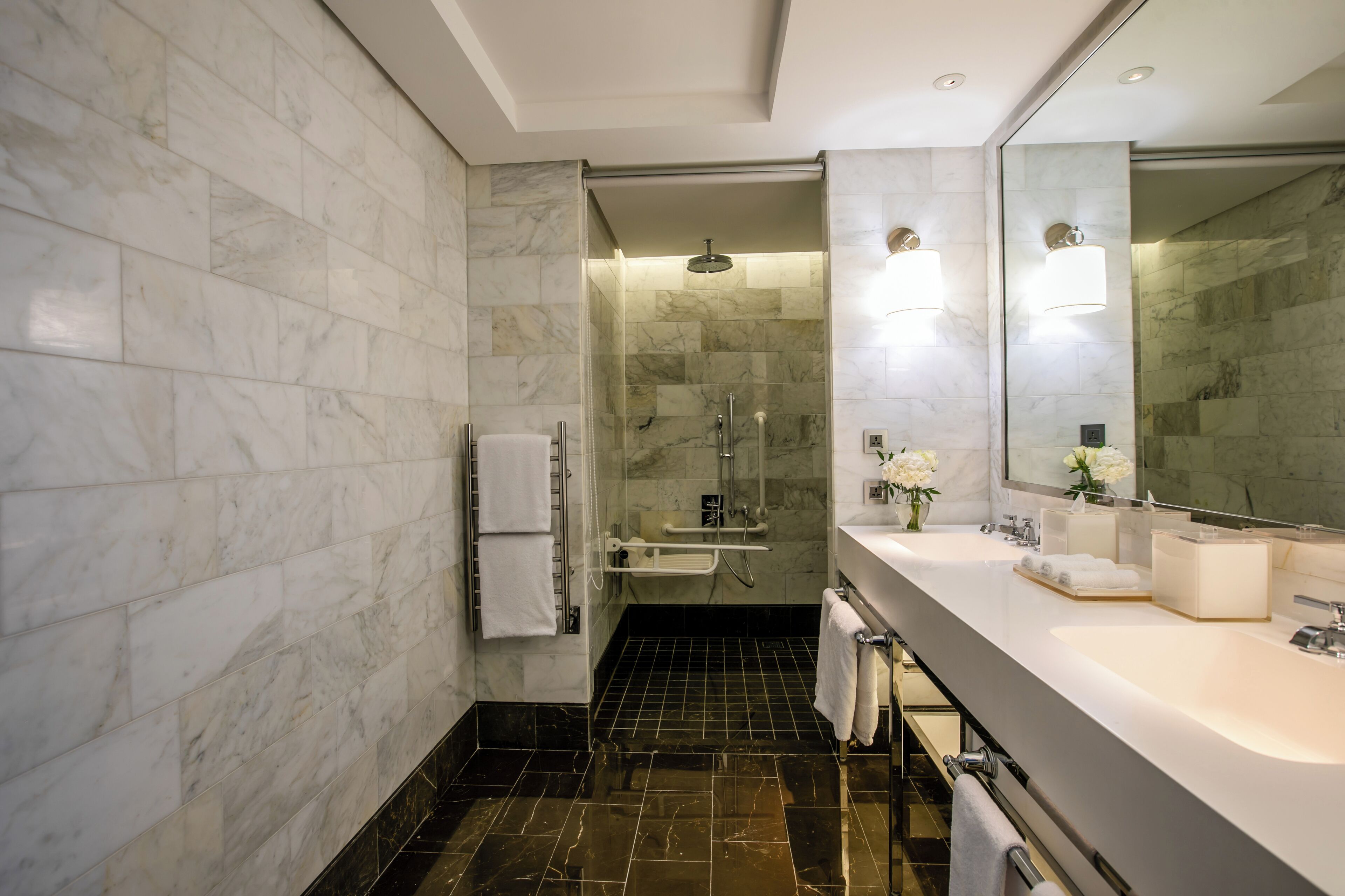 A modern bathroom with a large mirror, dual sinks, and a shower area.