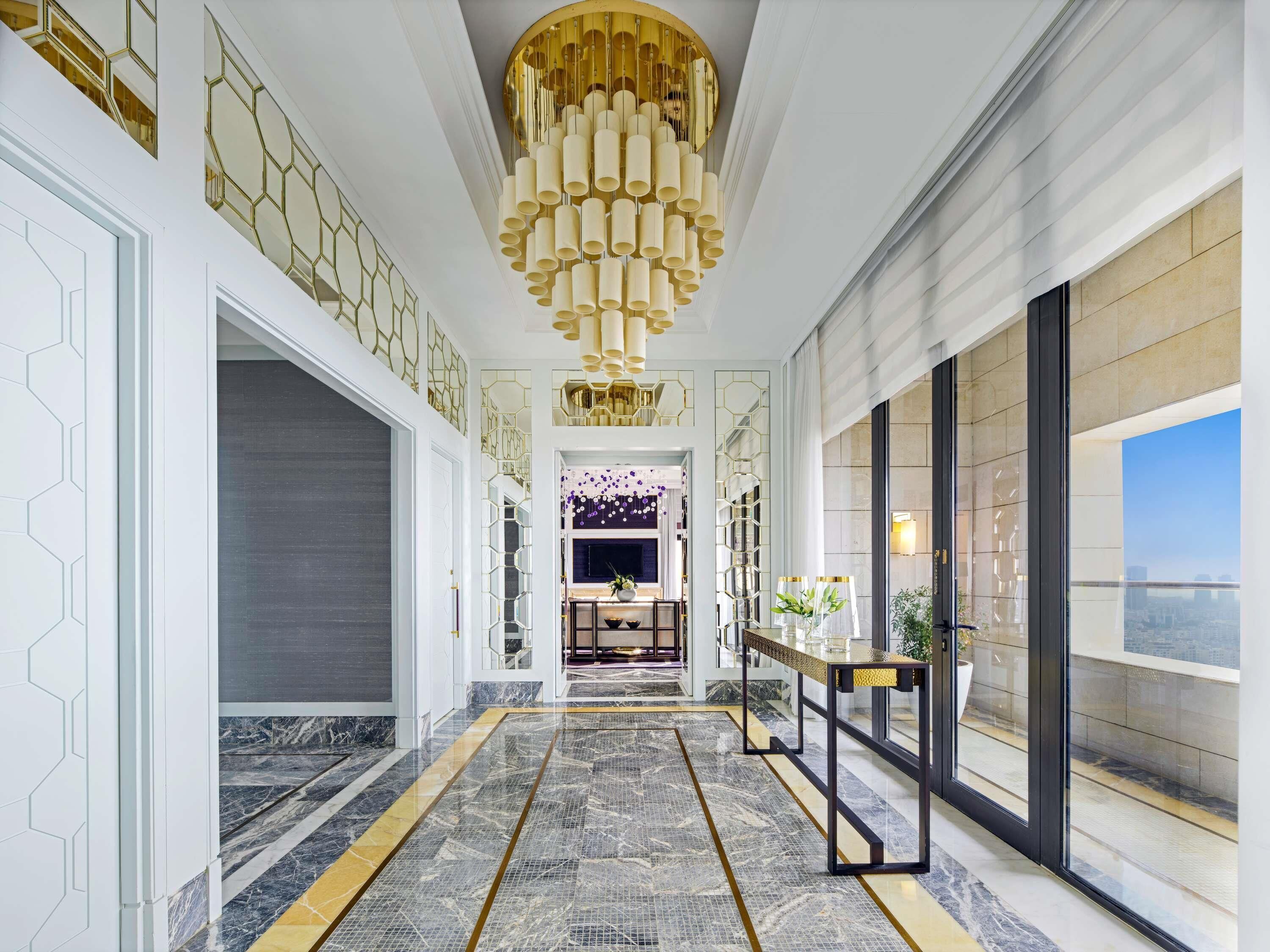 A modern hotel lobby with a marble floor, a large chandelier, and a view of the city.