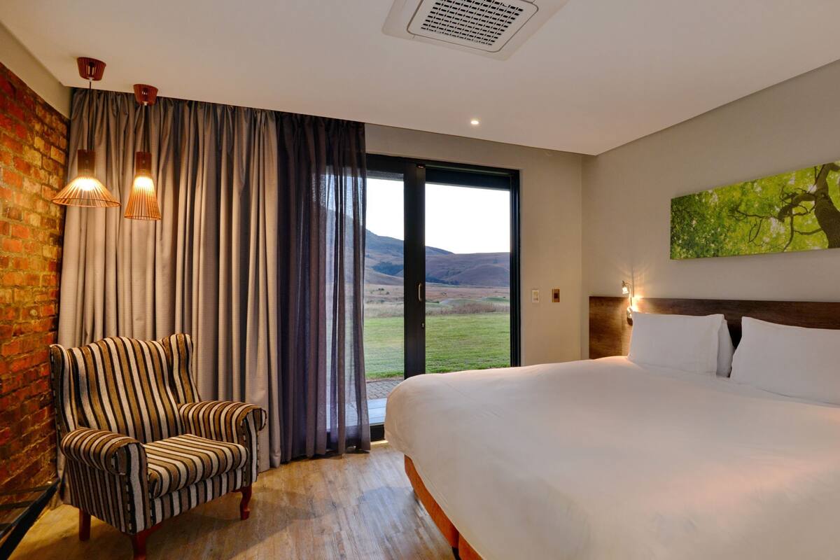 Ein Hotelzimmer mit einem großen Bett, einem Sessel, einem Gemälde und Blick ins Freie.