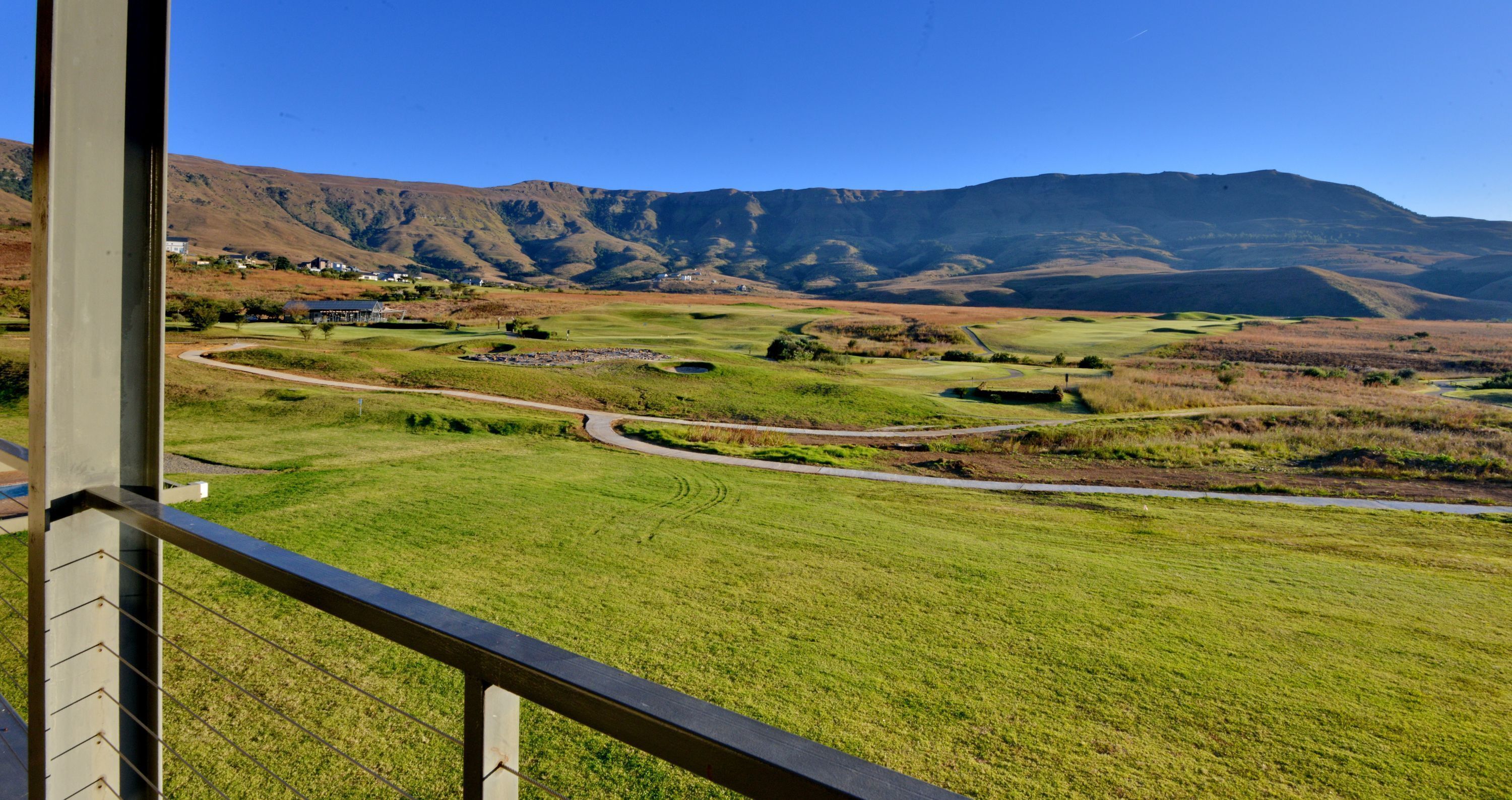 A view of a golf course with a winding path, a small pond, and distant mountains.