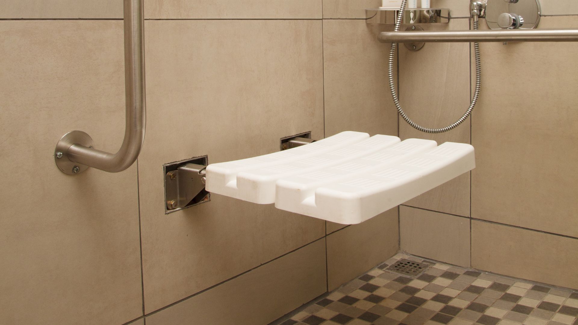 A shower area with a white shelf, a showerhead, and a checkered floor.
