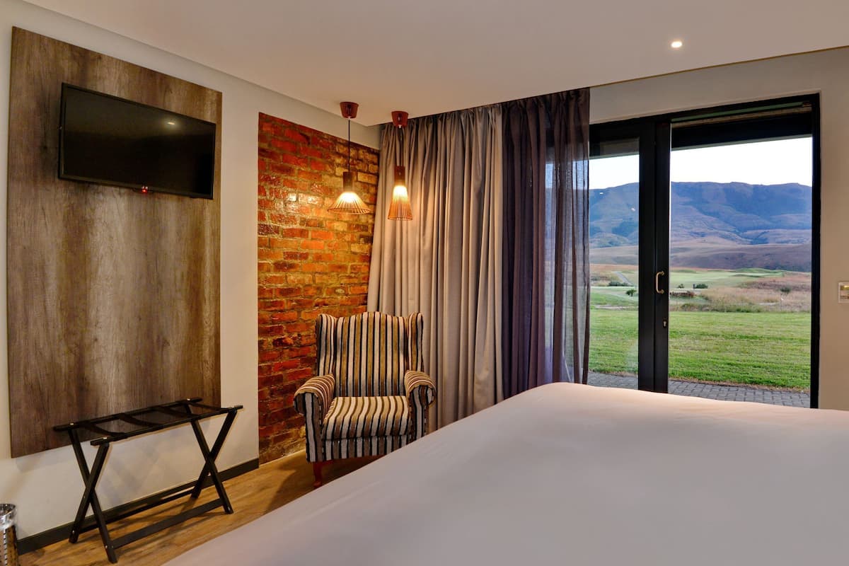 Ein Hotelzimmer mit einem großen Bett, einem an einer Ziegelwand befestigten Fernseher, einem gestreiften Sessel und Blick ins Freie.
