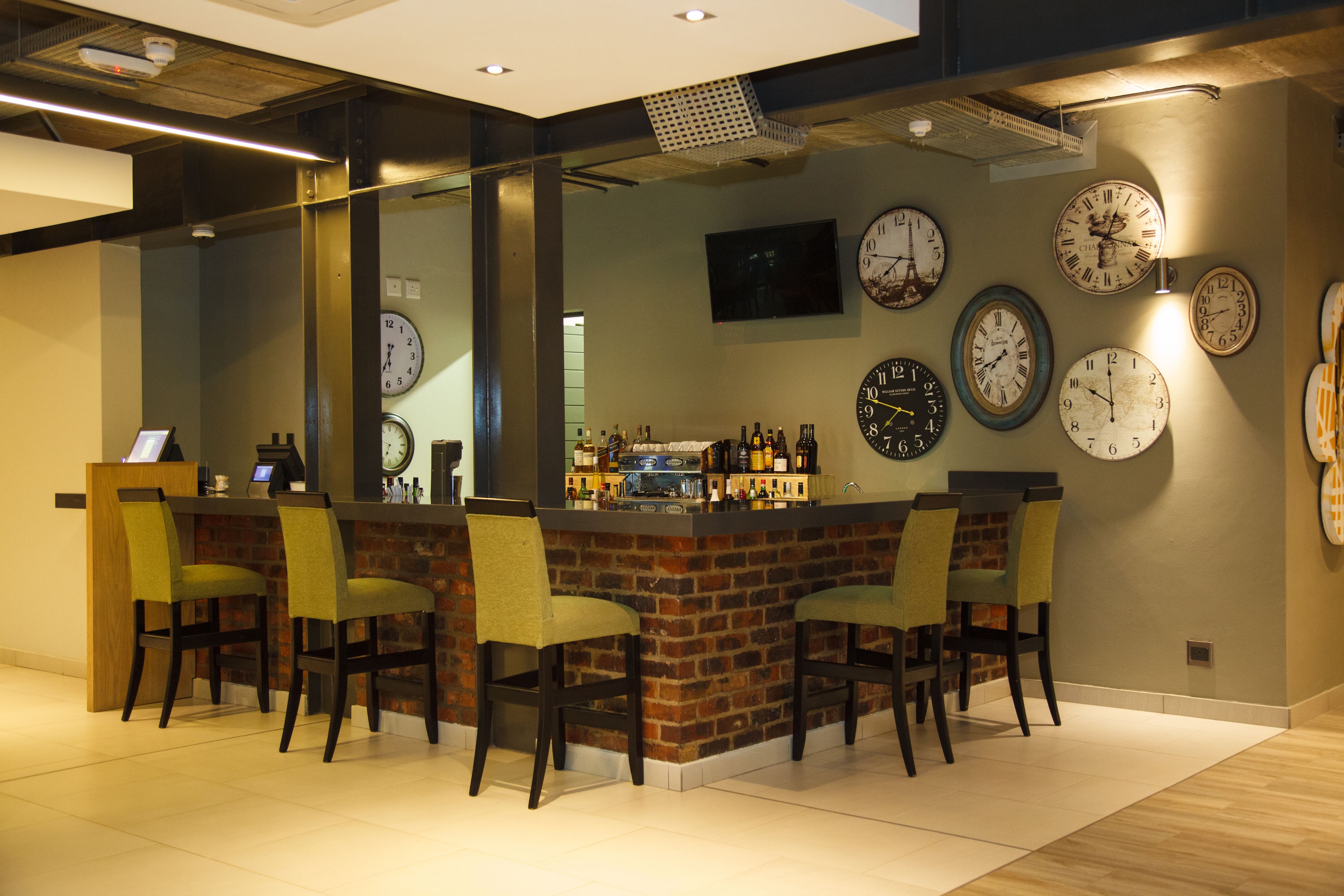 A bar area with a brick wall, multiple clocks, and bar stools.