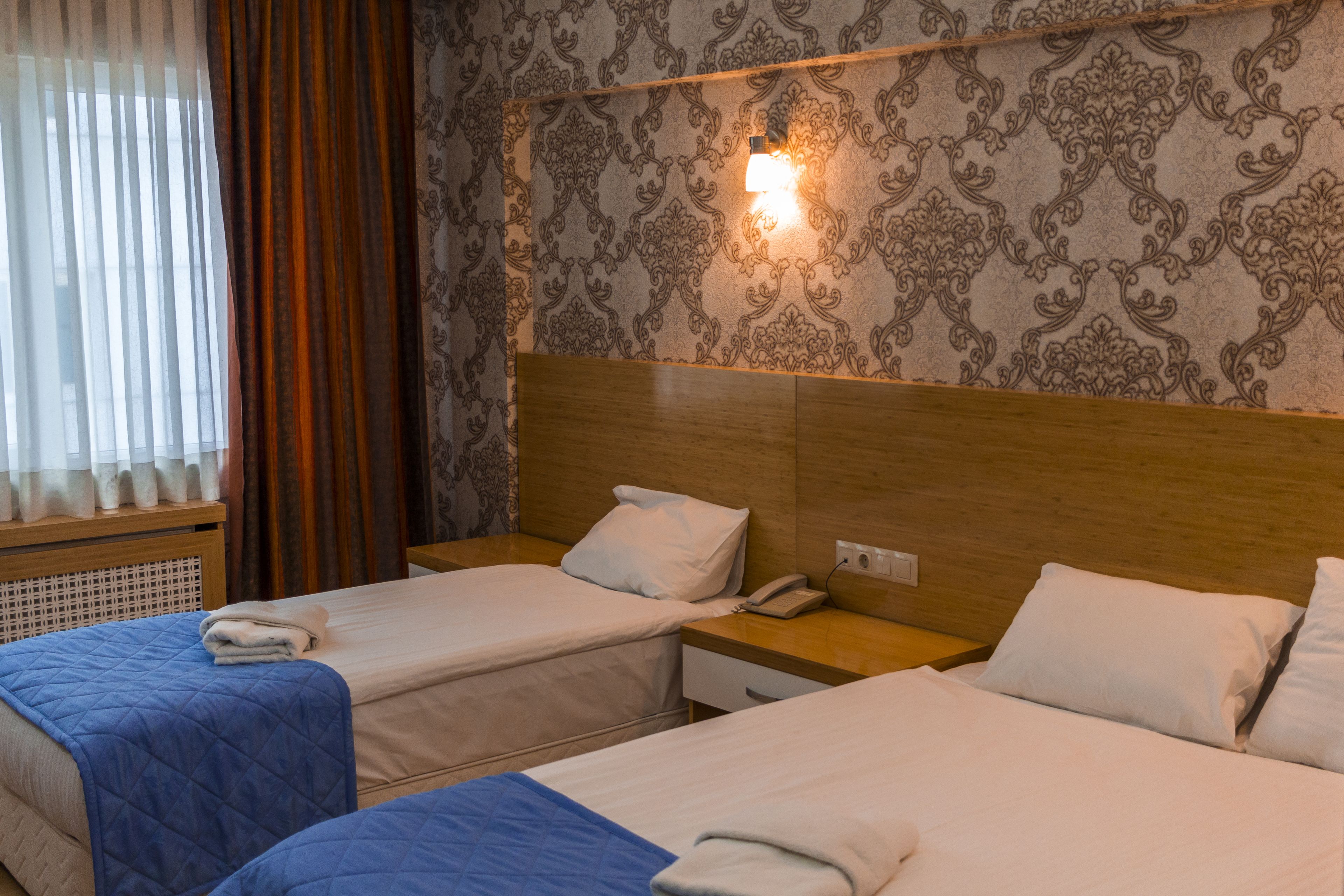 A hotel room with two beds, a wooden headboard, a nightstand with a phone, and a wall-mounted light fixture.