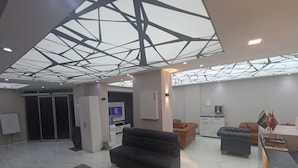 A modern lobby with a geometric ceiling, a seating area with sofas, a reception desk, and a flag display. - Peracity Hotel (Ankara)