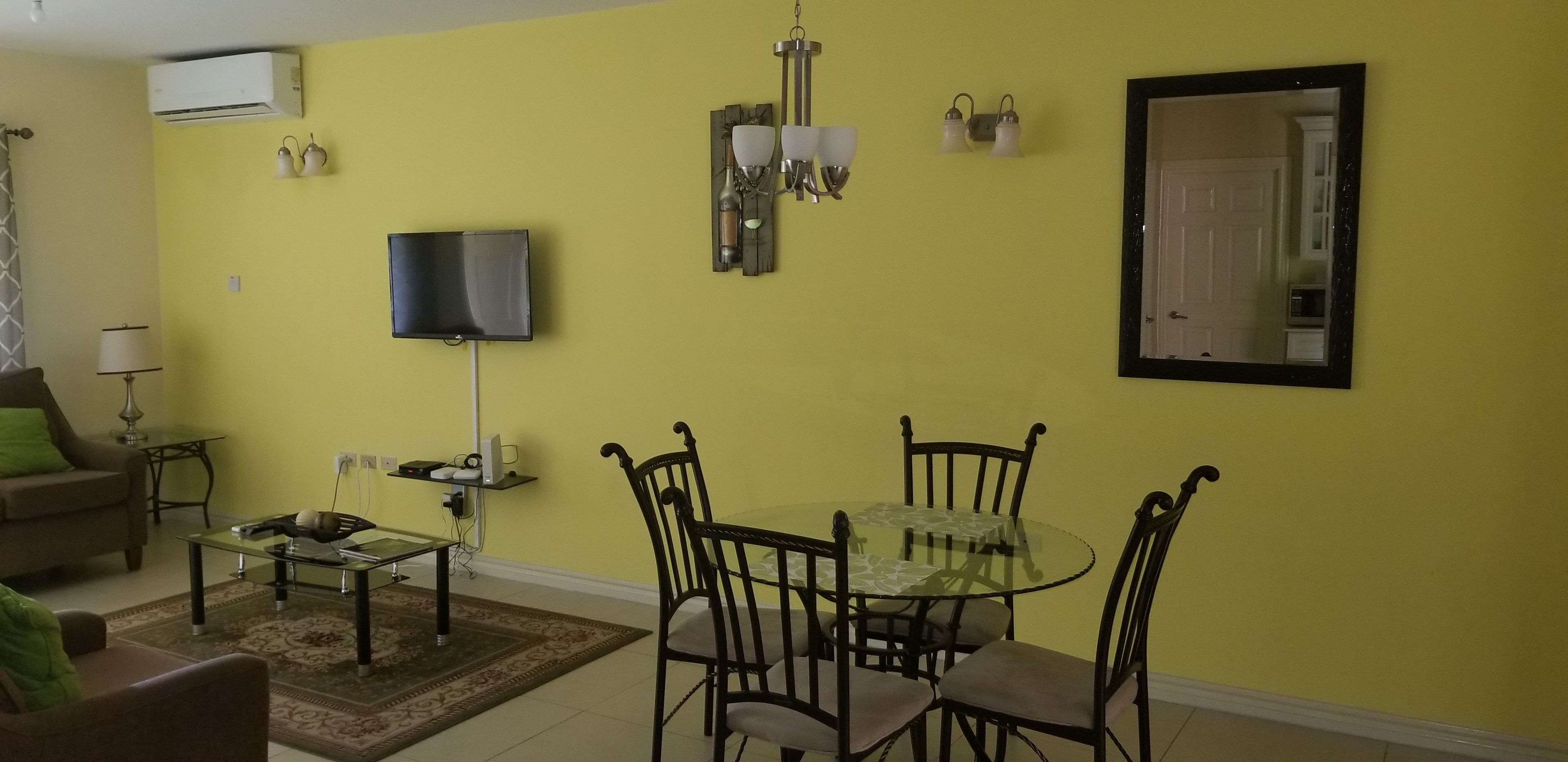 A living room with a sofa, coffee table, TV, and a dining area with a glass table and chairs.