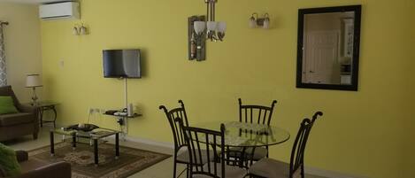 A living room with a sofa, coffee table, TV, and a dining area with a glass table and chairs.
