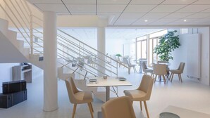 Un intérieur moderne avec un escalier, un coin repas et de grandes fenêtres.