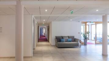Een moderne lobby met een centrale gang, een bank met kussens en een potplant.