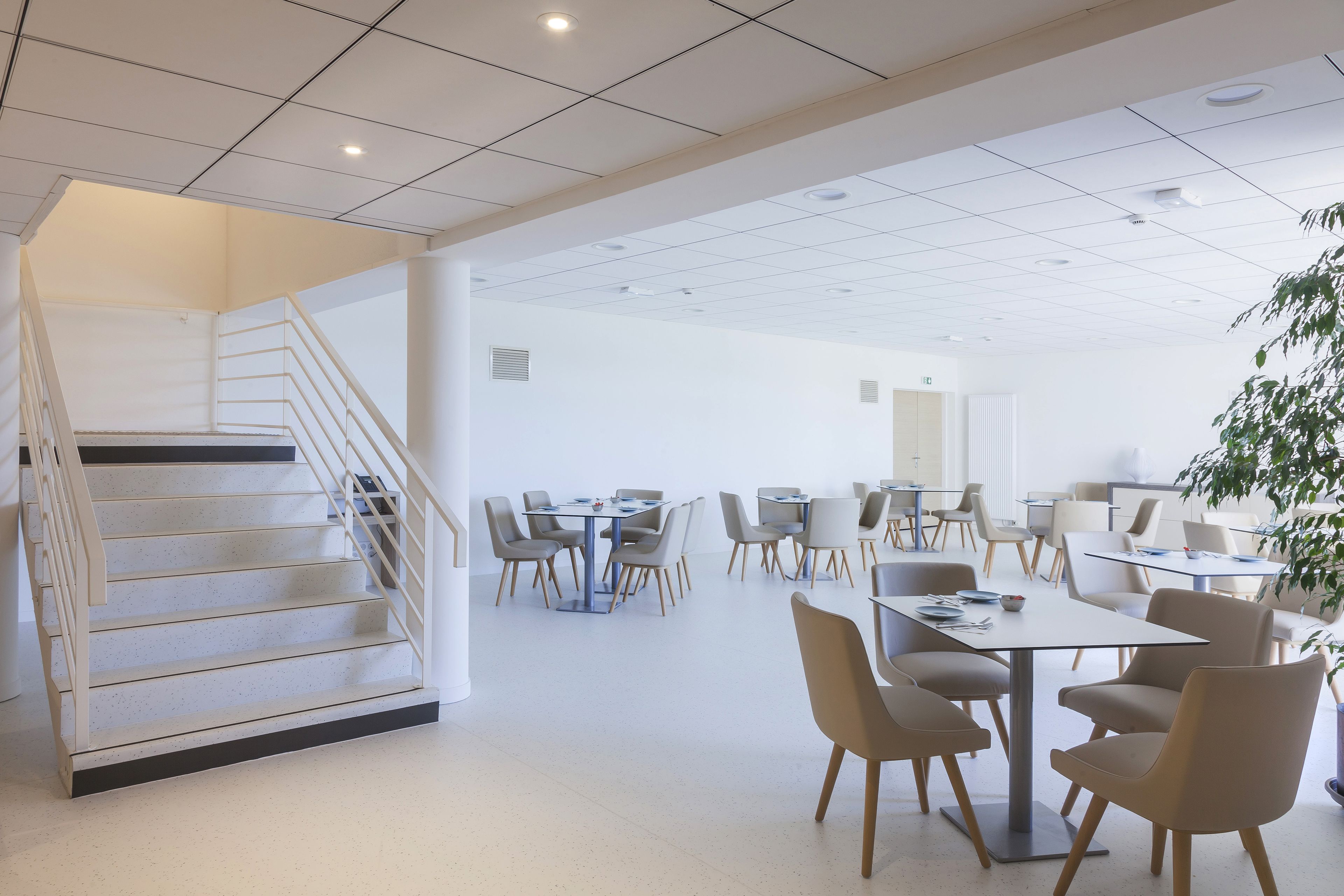 A spacious, modern dining area with multiple tables and chairs, a staircase, and a ceiling with recessed lighting.