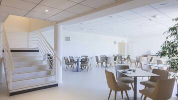 A spacious, modern dining area with multiple tables and chairs, a staircase, and a ceiling with recessed lighting.