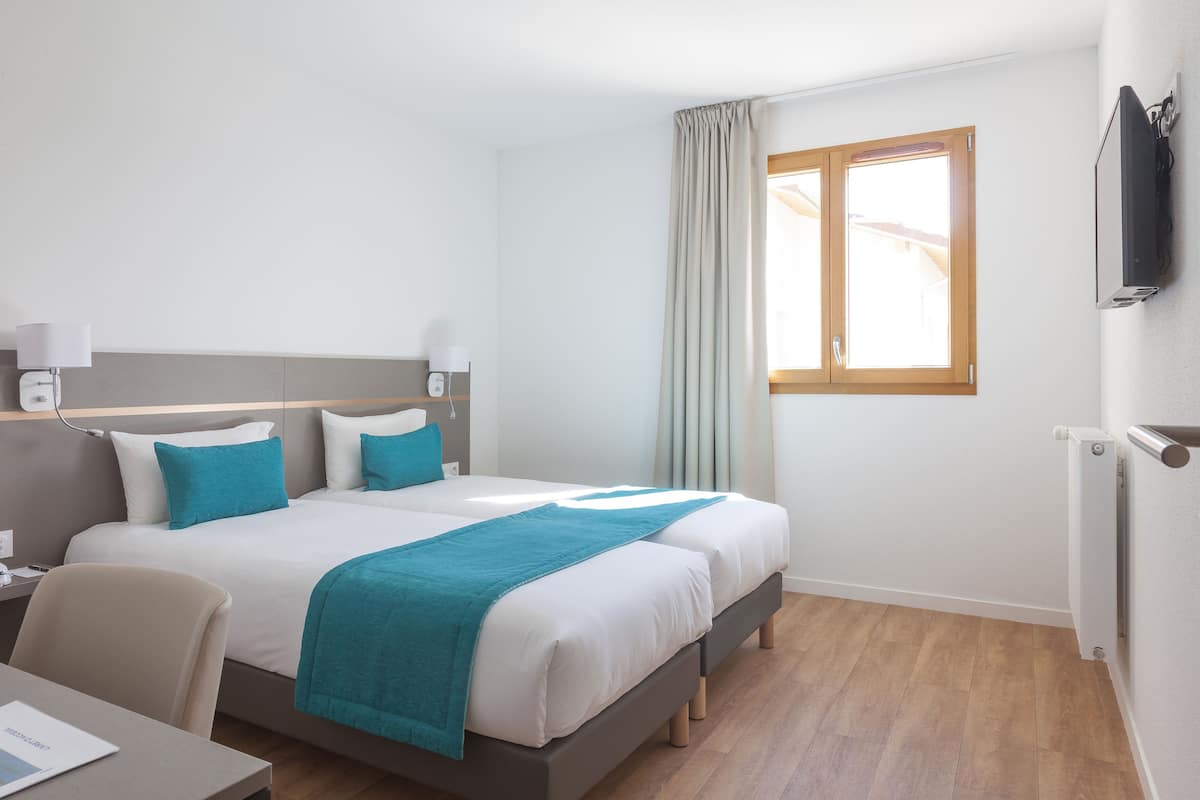 Ein Hotelzimmer mit einem großen Bett, einem Schreibtisch, einem Stuhl, einem an der Wand befestigten Fernseher und einem Fenster mit Vorhängen.