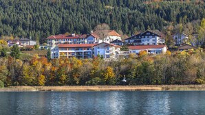 Un hôtel situé au bord d’un lac, composé de plusieurs bâtiments, adossé  à une colline boisée et offrant une vue dégagée sur le lac.