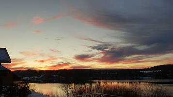 Auringonlasku järven yllä, ja etualalla näkyy talo.