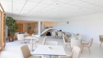 Un espace de salle à manger spacieux et moderne, avec plusieurs tables et chaises, un escalier et une grande plante en pot.
