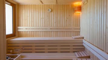 A wooden sauna with benches and a window, featuring a wall-mounted heater and a wall-mounted light fixture.