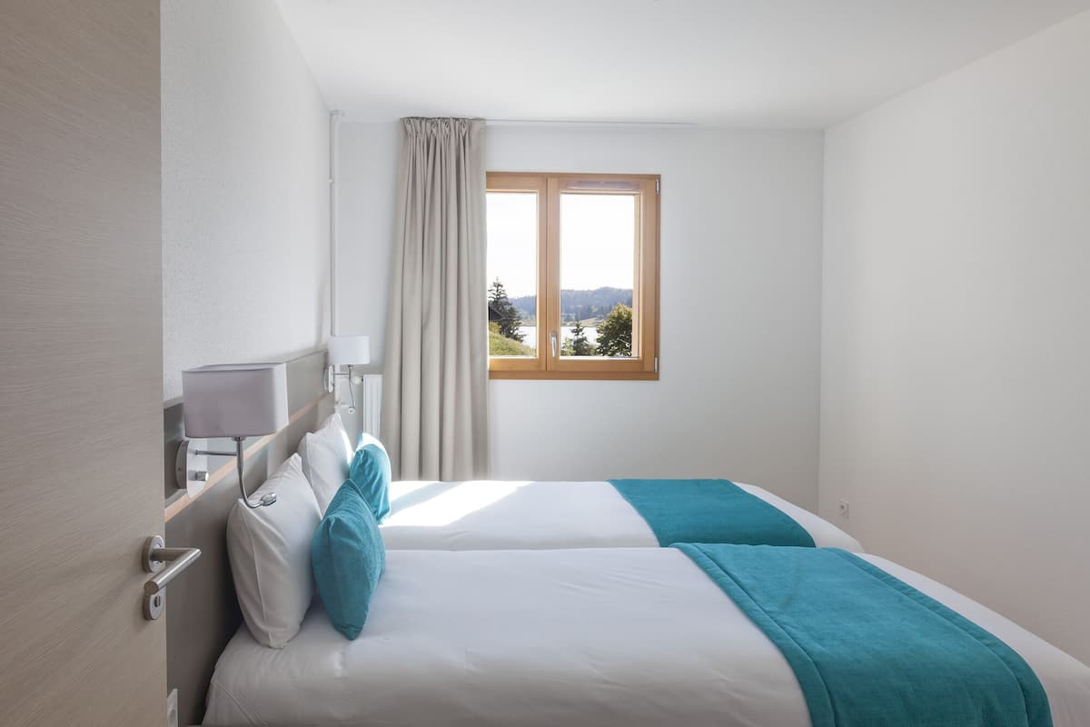 Ein Hotelzimmer mit zwei Betten, einem Fenster mit Blick ins Freie, einer Lampe und einem Vorhang.