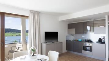 A modern kitchen with a flat-screen TV, a dining area with a table and chairs, and a view of a lake through large windows.