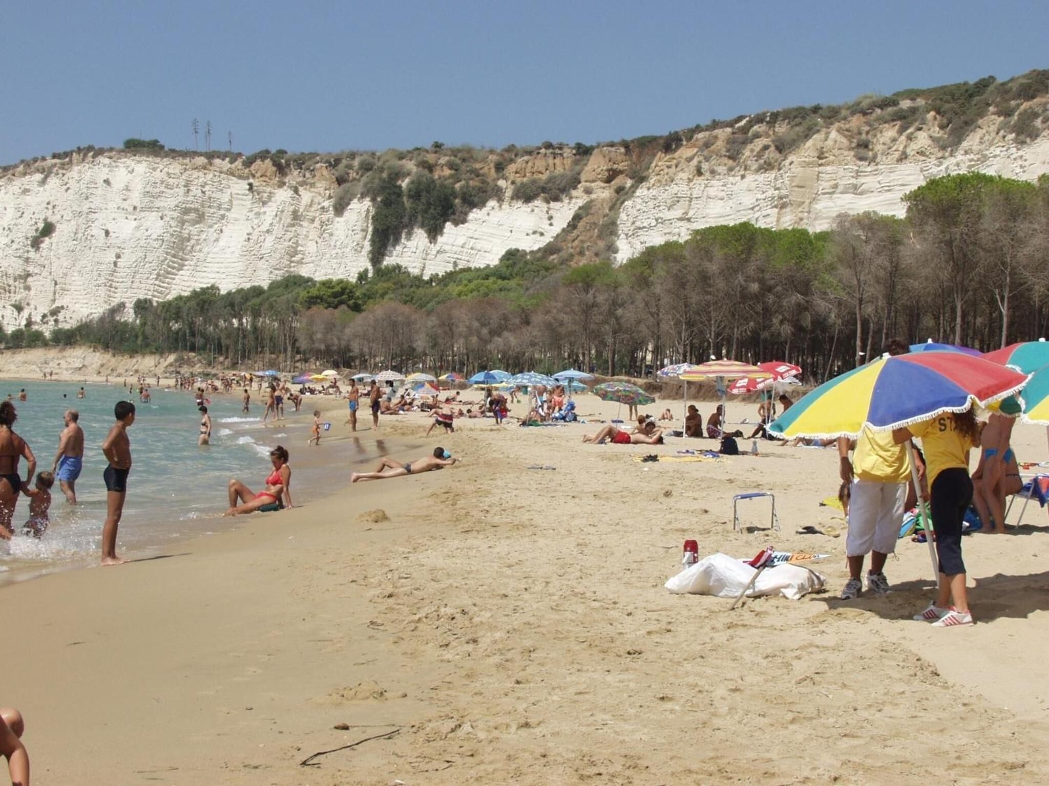 A beach with people sunbathing and swimming, a sandy shore, and cliffs in the background.