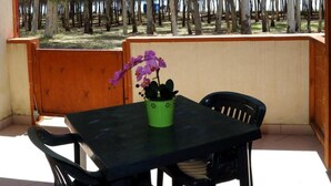 A covered patio with a table and chairs, a potted orchid, and a view of trees. - Eraclea Minoa Village (Cattolica Eraclea)