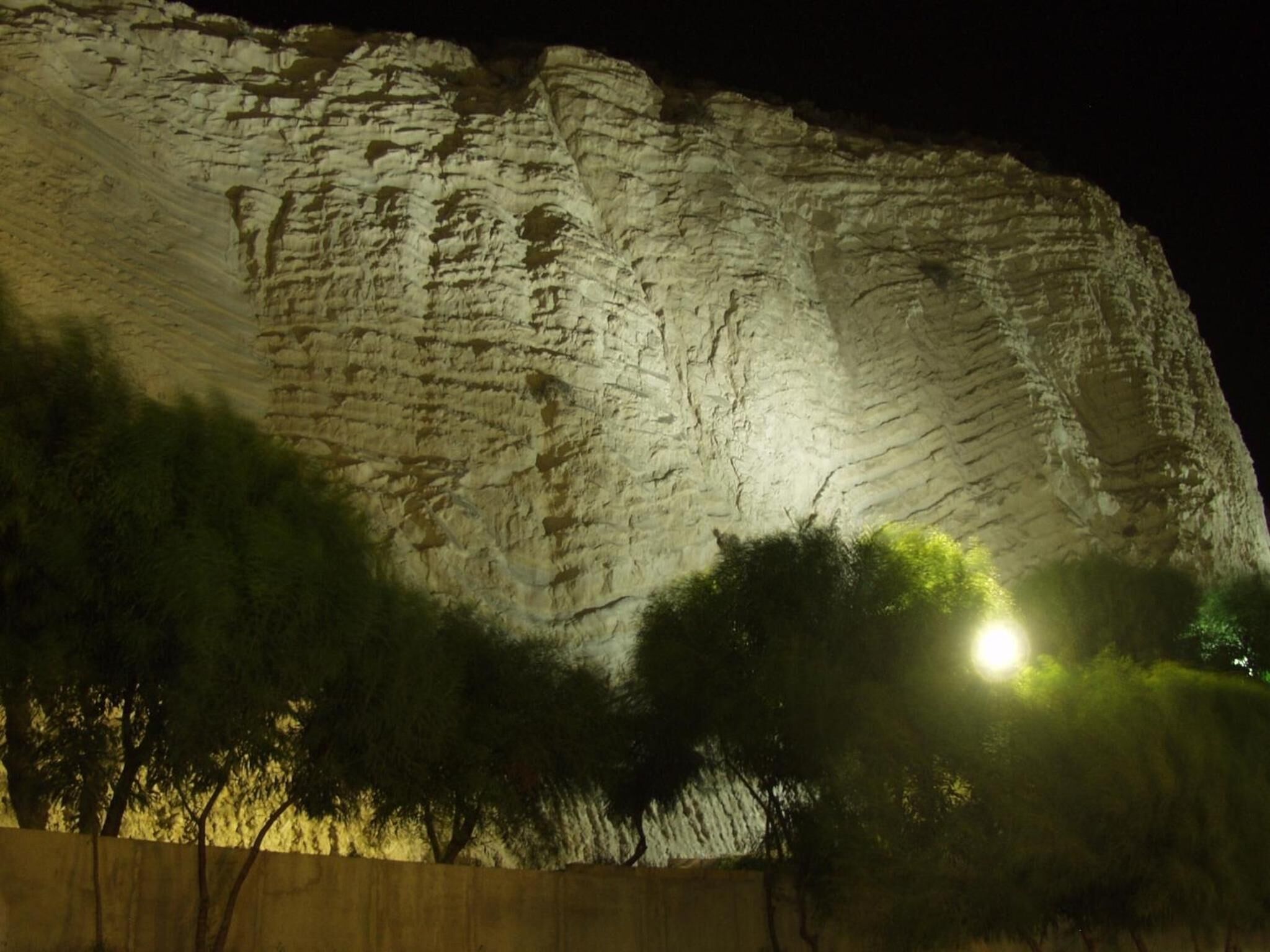Une grande formation rocheuse illuminée la nuit, avec un lampadaire à proximité.
