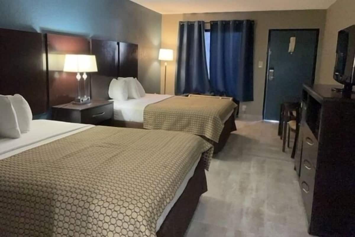 A hotel room with two beds, a desk, a chair, a TV, and a door.