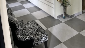 Un área de recepción con suelo a cuadros, un mostrador, un microondas, una computadora portátil, un jarrón con flores y una silla estampada.