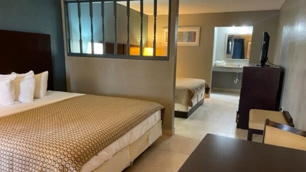 Habitación de hotel con cama, una mesita, una silla, un escritorio, un espejo y un baño visible a través de una puerta abierta.