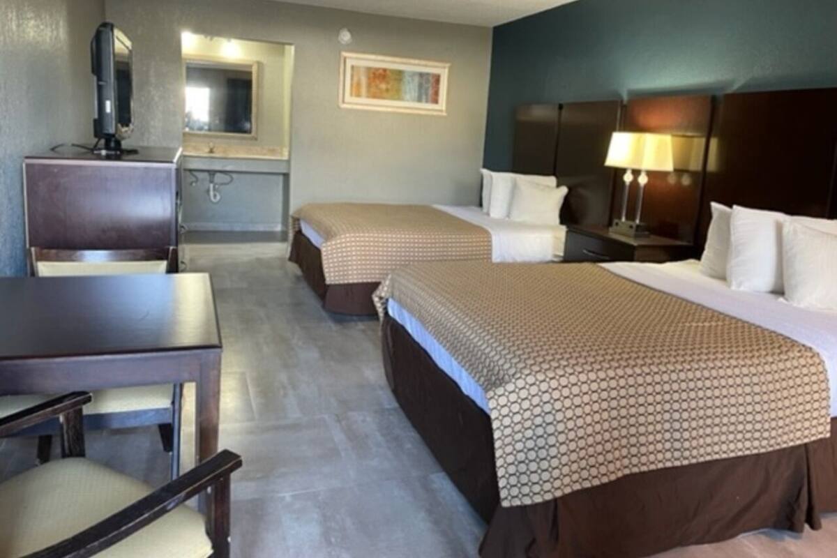 A hotel room with two beds, a desk, a chair, a TV, a mirror, and a lamp.