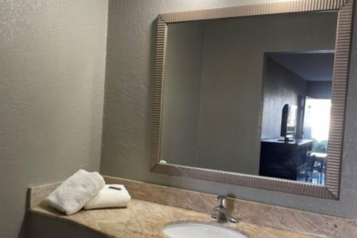 A bathroom with a sink, mirror, towel, and a visible pipe.
