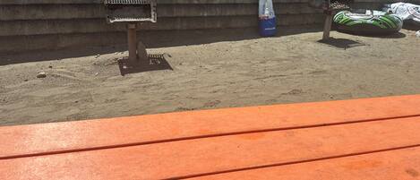 A sandy outdoor area with a grill, a table, and a green inflatable object.
