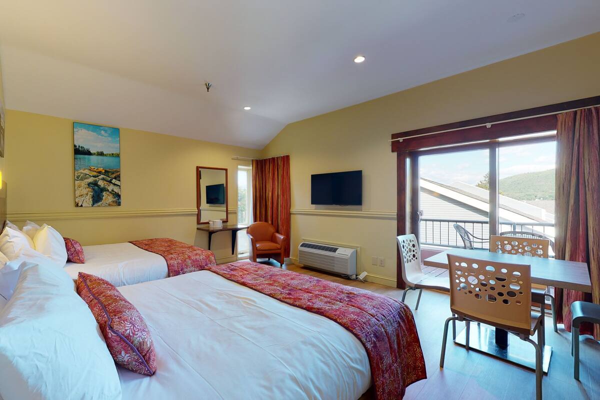 A hotel room with two beds, a desk, a chair, a television, and a balcony with a view.