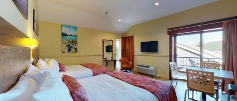 A hotel room with two beds, a desk, a chair, a television, and a balcony with a view.