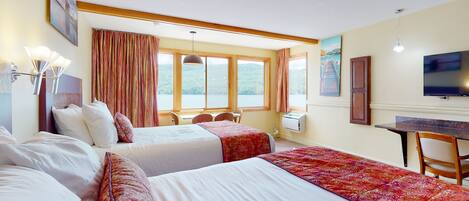 Une chambre d’hôtel avec deux lits, une table à manger, un téléviseur et une fenêtre donnant sur un lac.