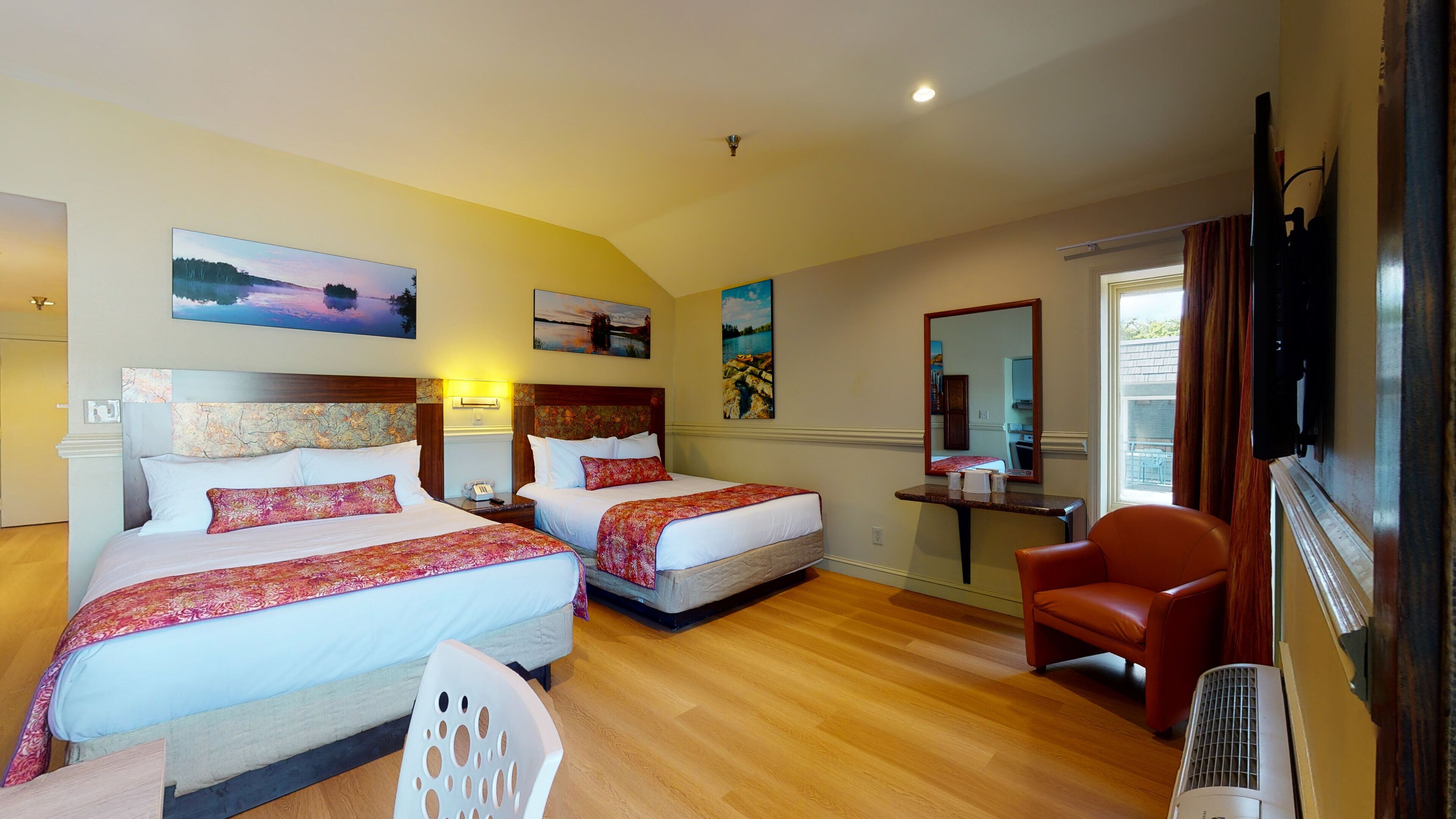 Habitación de hotel con dos camas, una zona de estar con una silla, televisor y obras de arte en las paredes.