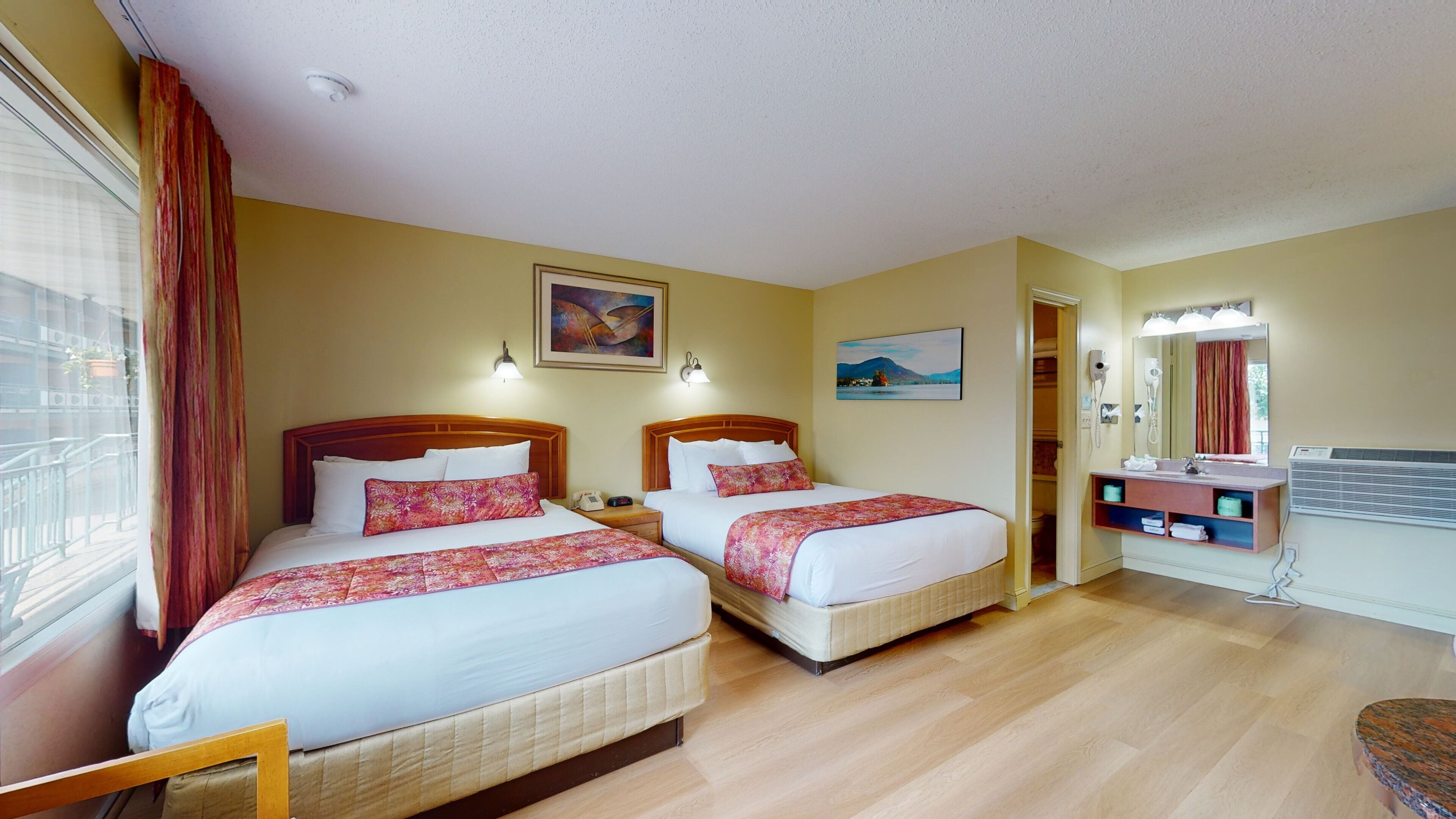 A hotel room with two beds, a bathroom with a mirror, and a window with curtains.
