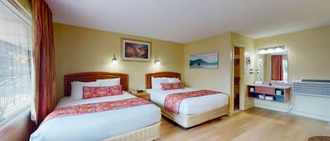 A hotel room with two beds, a bathroom with a mirror, and a window with curtains.