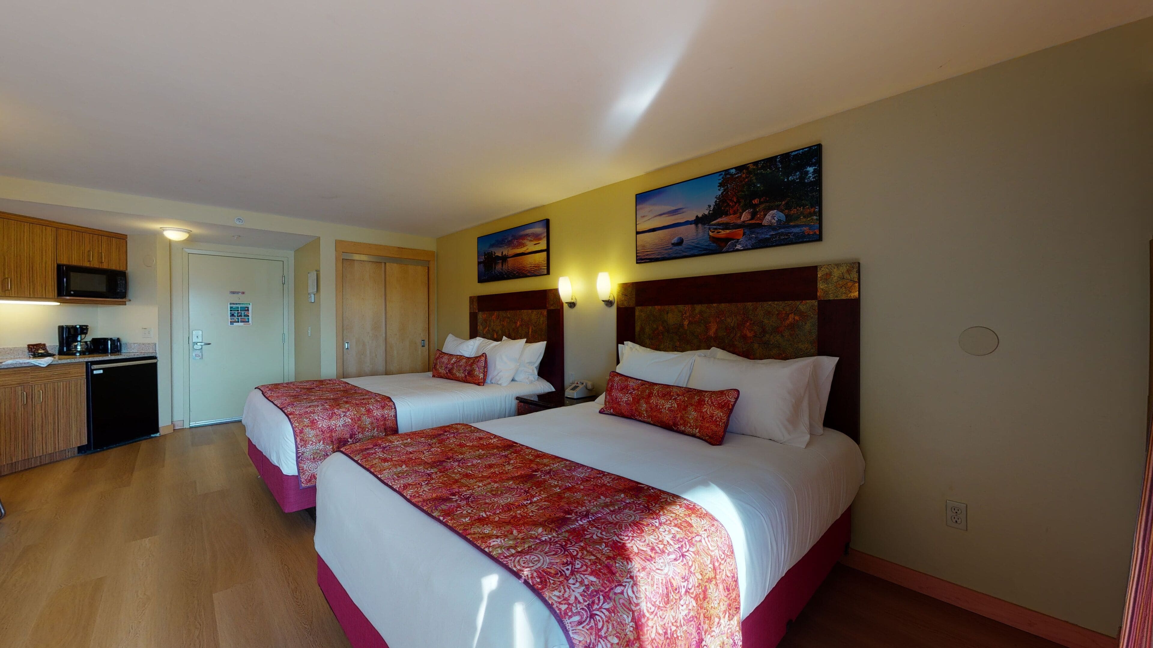 Quarto de hotel com duas camas, uma cozinha compacta e um quadro na parede.