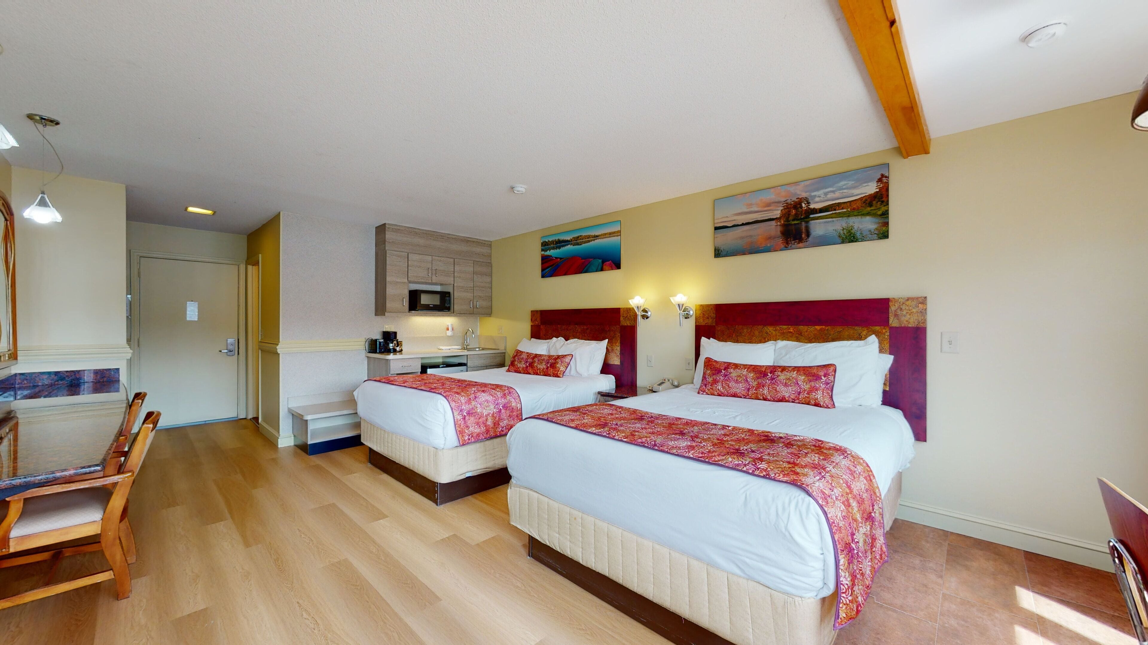 A hotel room with two beds, a kitchenette, a dining area, and a painting on the wall.