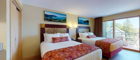A hotel room with two beds, a balcony, and artwork on the walls.