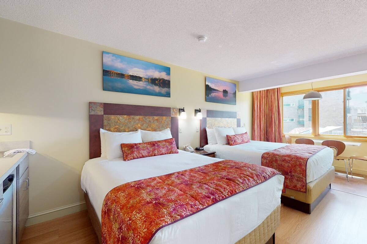 A hotel room with two beds, a desk, a chair, and a window with a view.