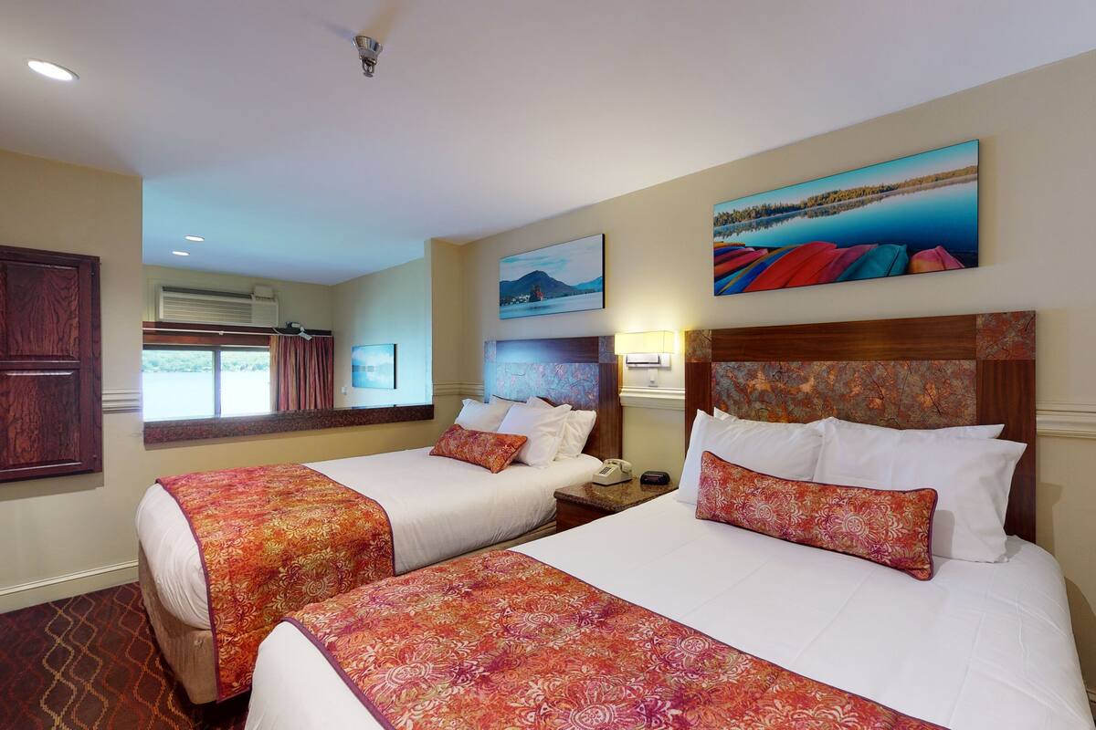 A hotel room with two beds, a large window, and artwork on the walls.