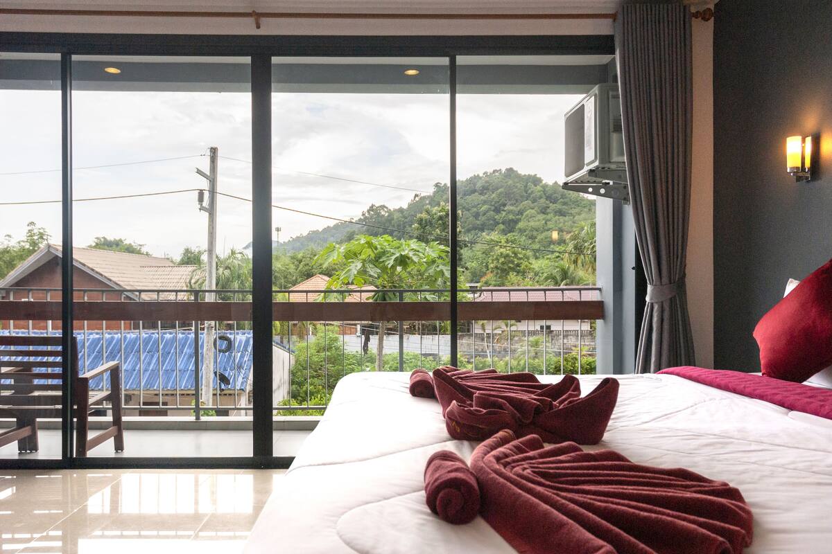 A hotel room with a large bed, a balcony with a view of a hill, and a television on the wall.
