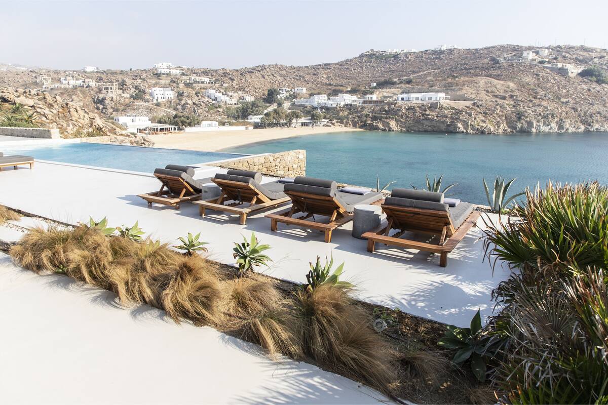 A poolside area with lounge chairs and a view of a coastal town.